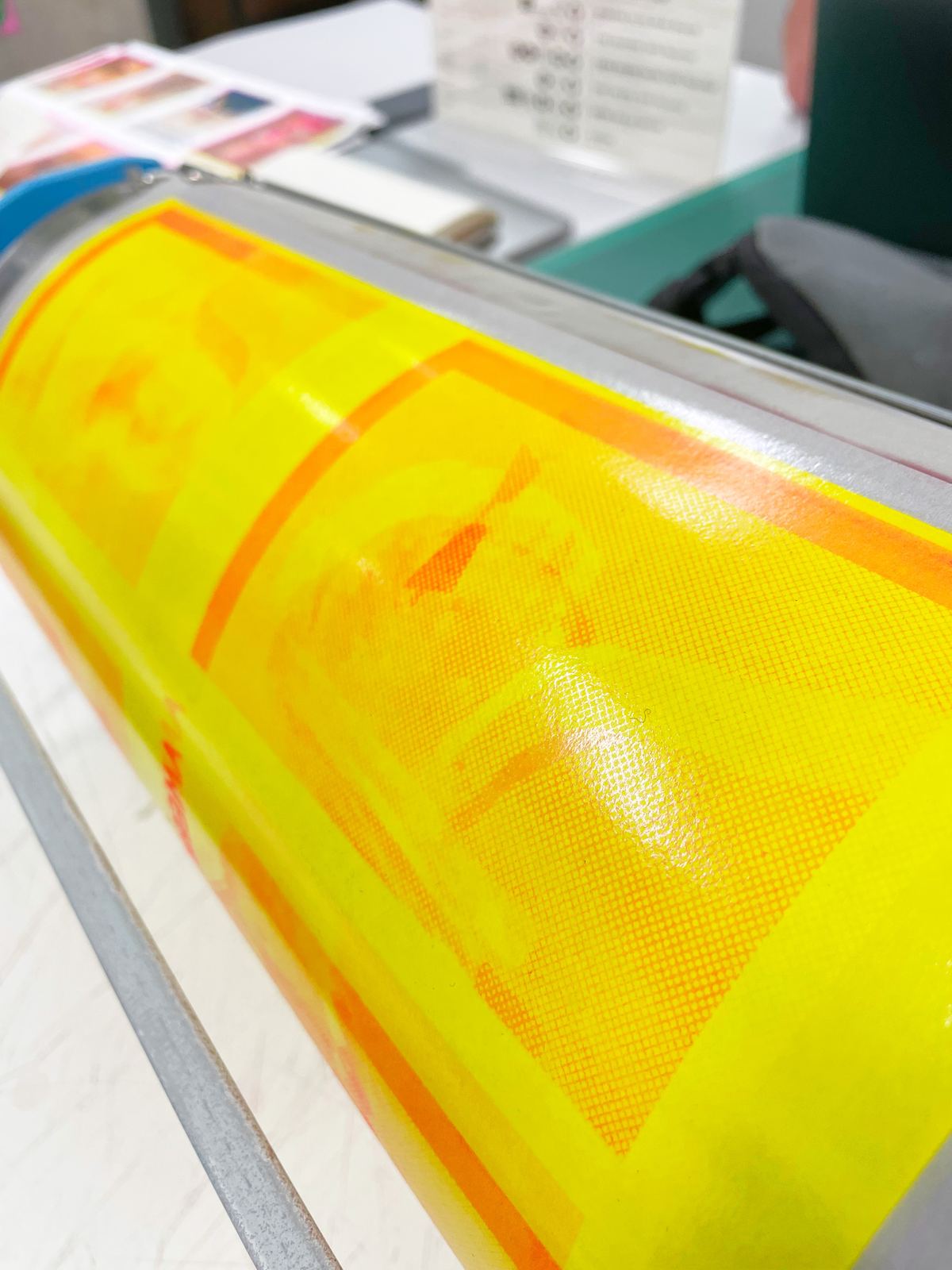 A yellow Riso master wrapped around the ink drum, the stencil's halftone grid showing through where the ink has pushed into it.